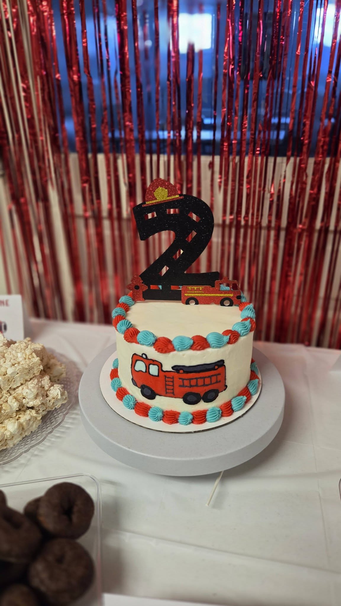 Two-tiered birthday cake decorated with a fire truck theme and a number 2 topper.