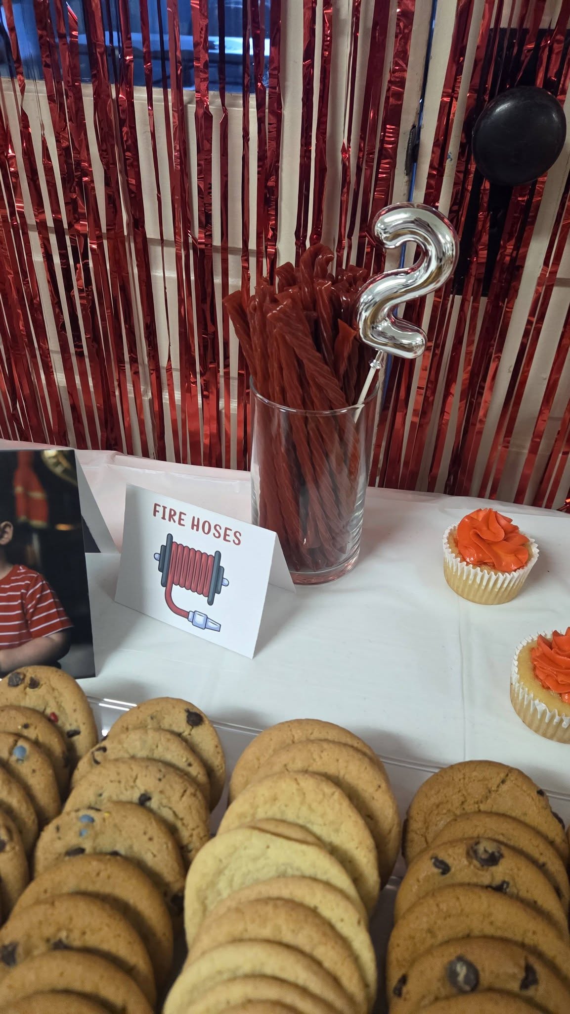 Table with cookie platters, cupcakes, and red licorice in a glass with a number two balloon for a party.