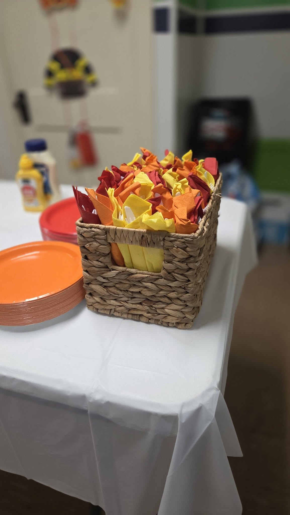 Woven basket filled with folded yellow, orange, and red party napkins on a table with plates