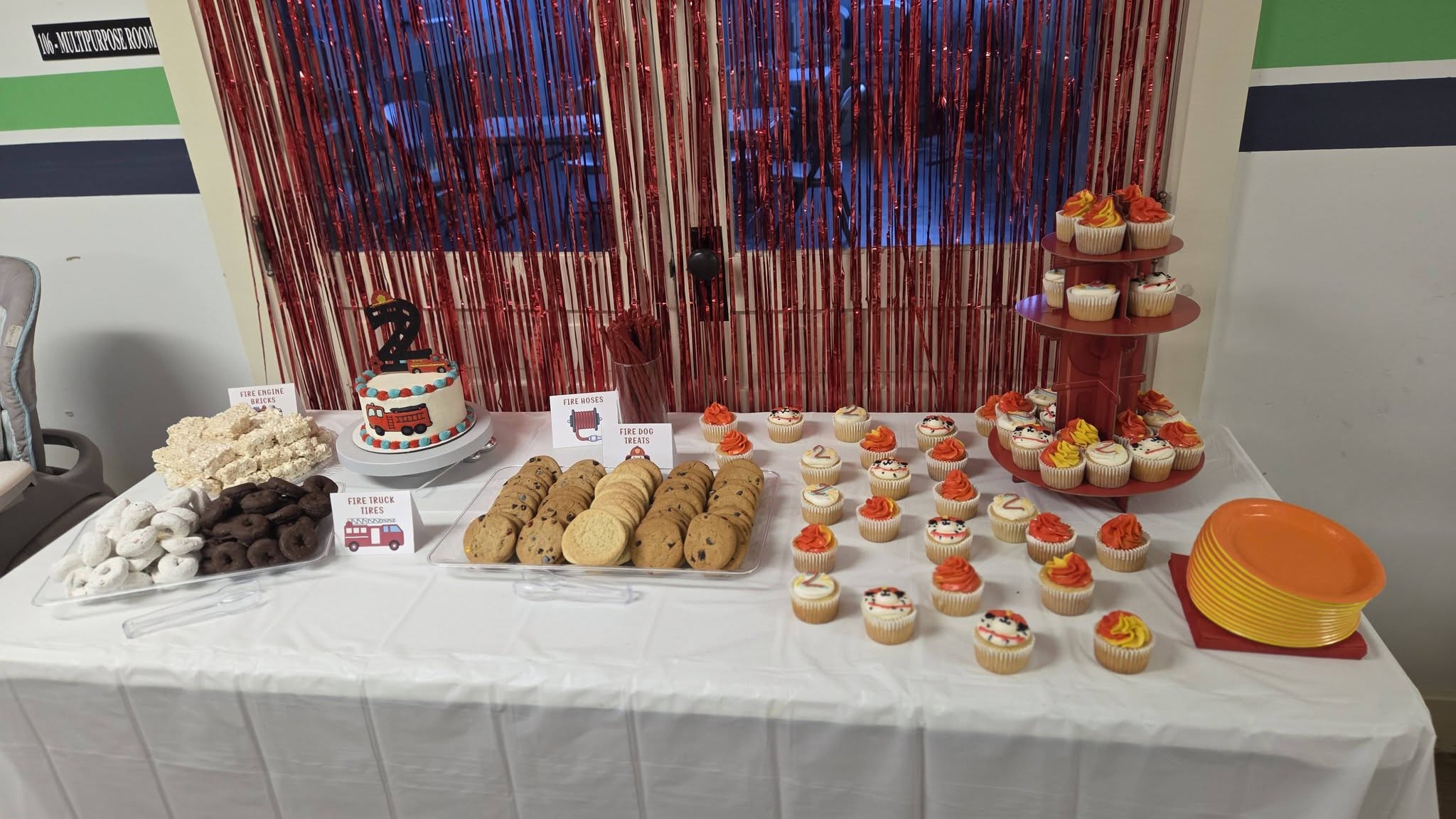Fire truck themed dessert table with cake, cupcakes, cookies, and snacks for a second birthday party.