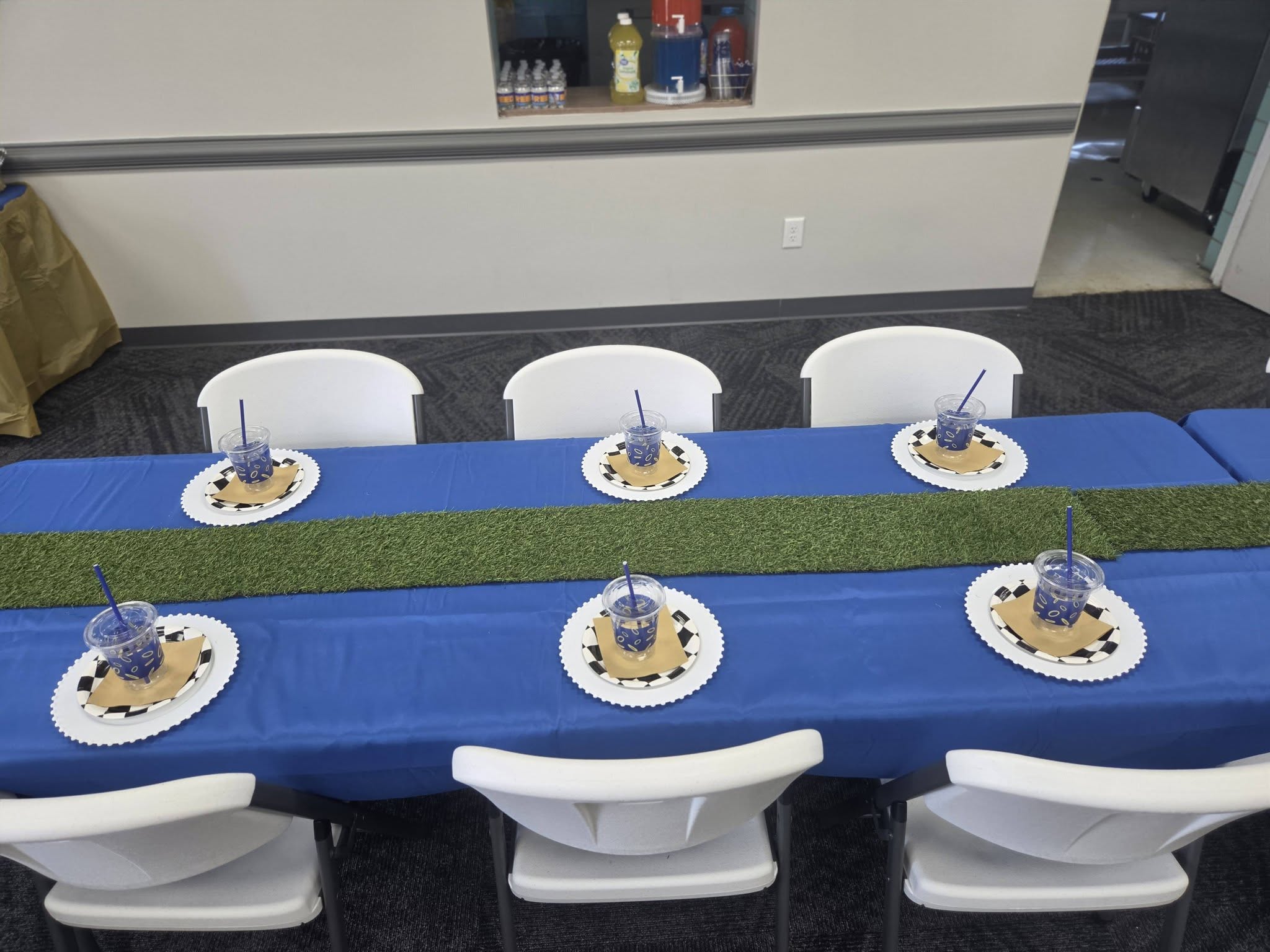 Table set for a party with blue tablecloth, grass table runner, and checkered party plates.