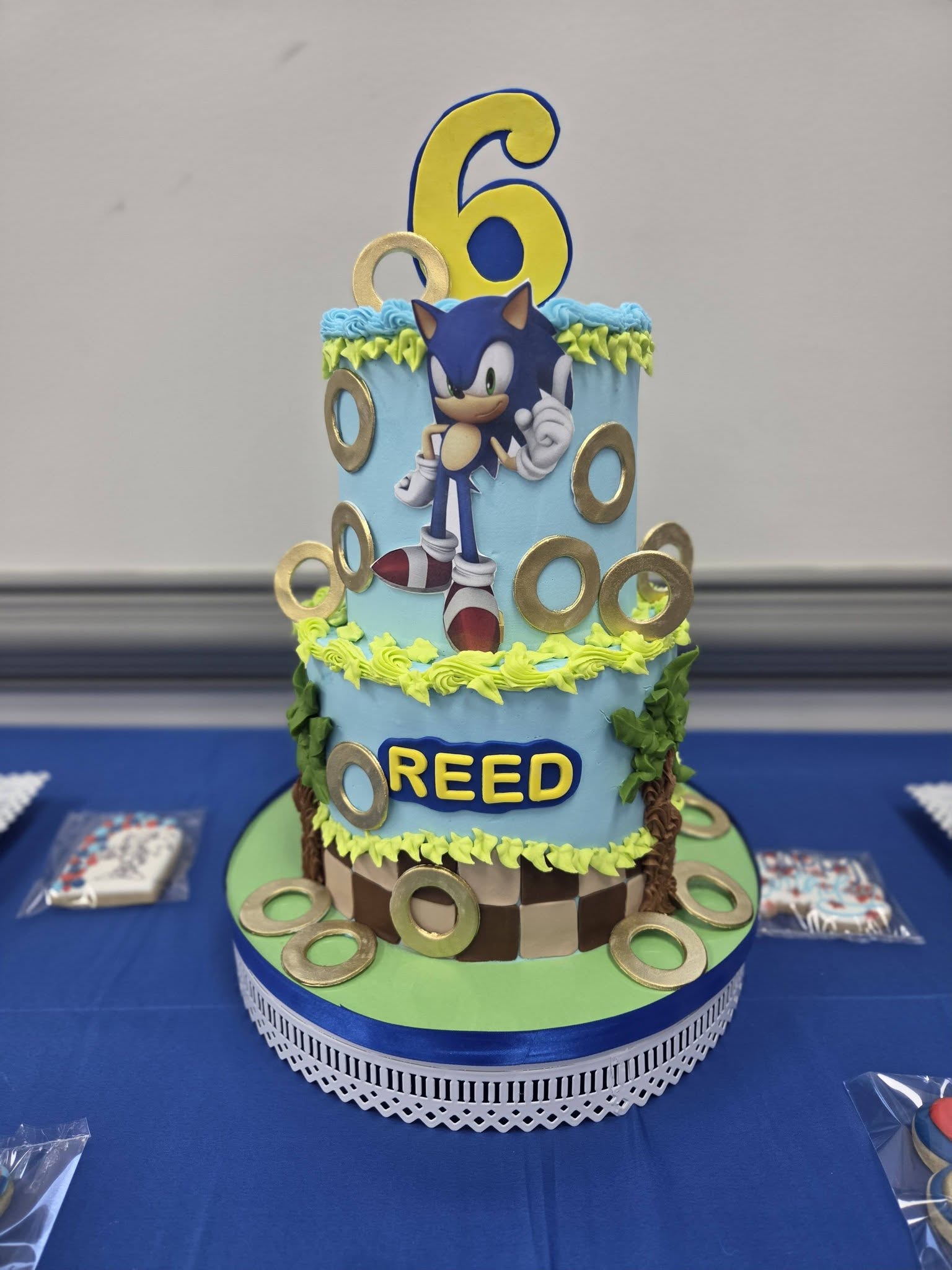 Two-tier blue Sonic the Hedgehog themed birthday cake with a large number 6 topper and the name Reed.