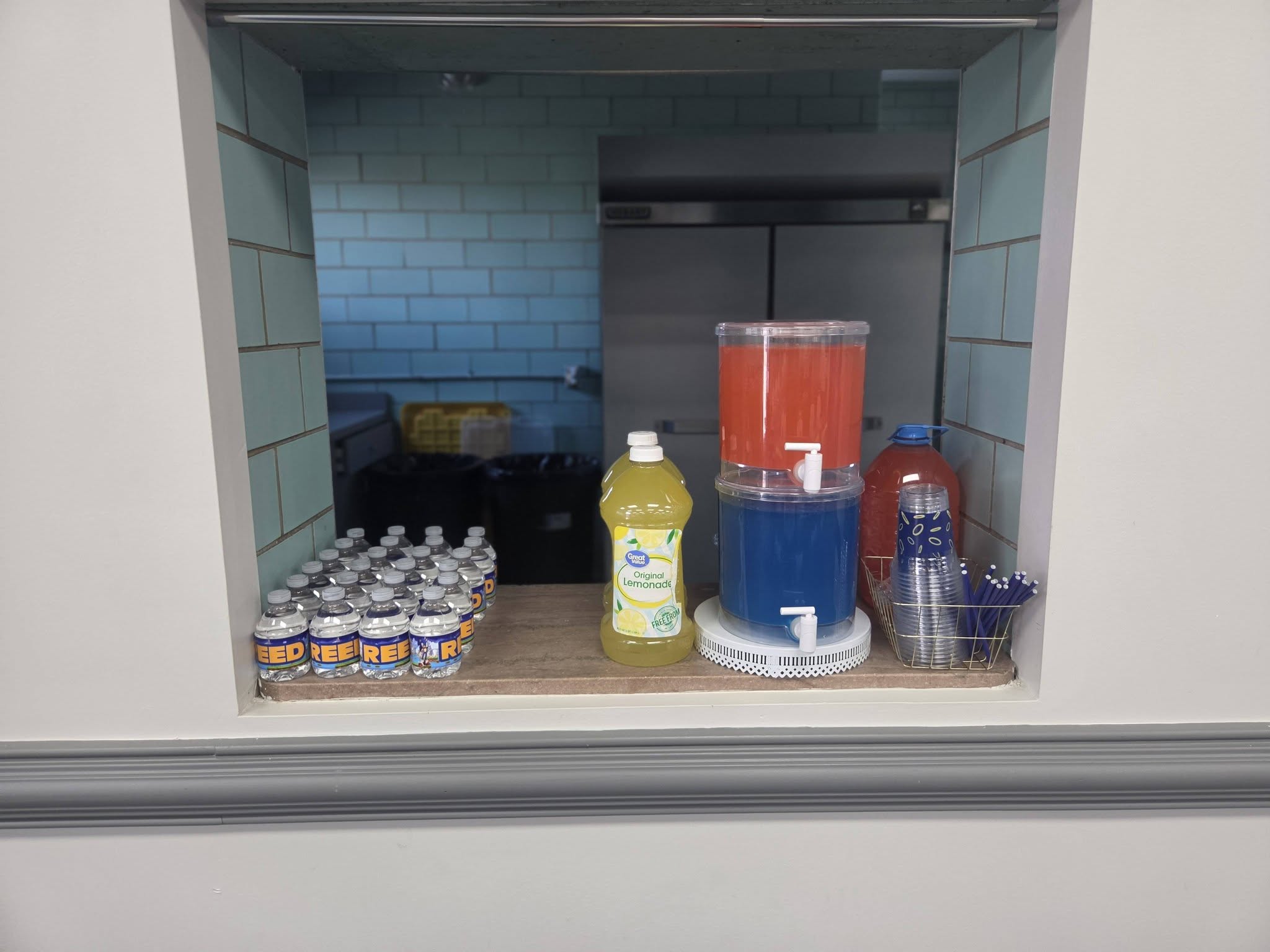 Drinks station with bottled water, lemonade, beverage dispensers, and stackable cups.
