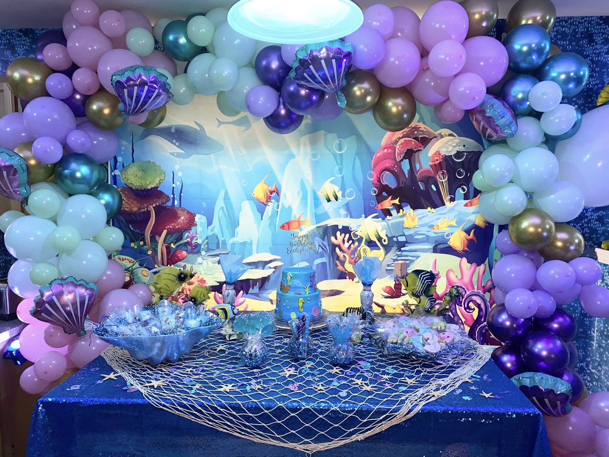 Underwater themed birthday dessert table with blue cake, balloons, and ocean decorations.