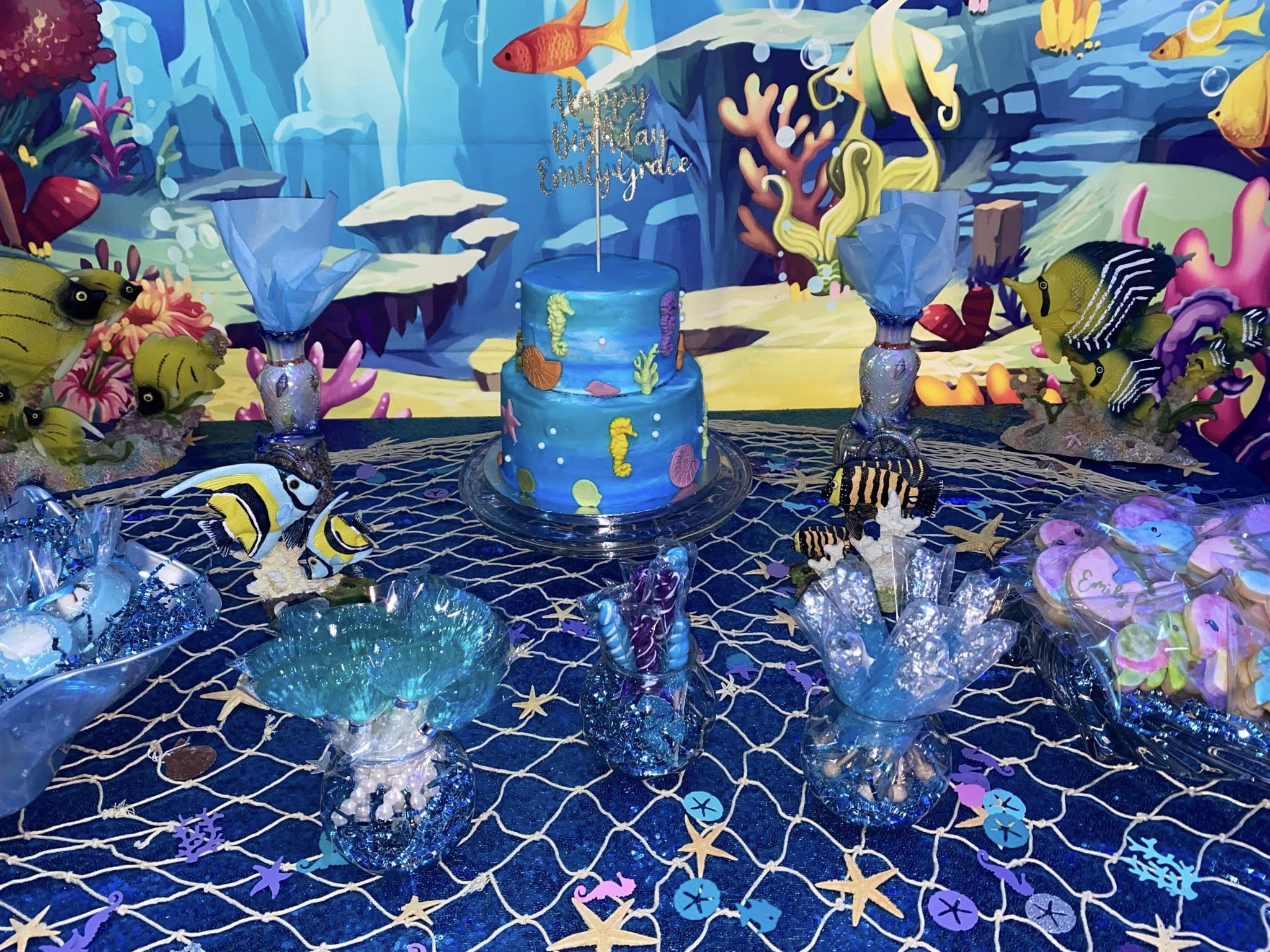 Two-tier blue ocean-themed birthday cake with sea creature decorations and an Emily Grace cake topper.