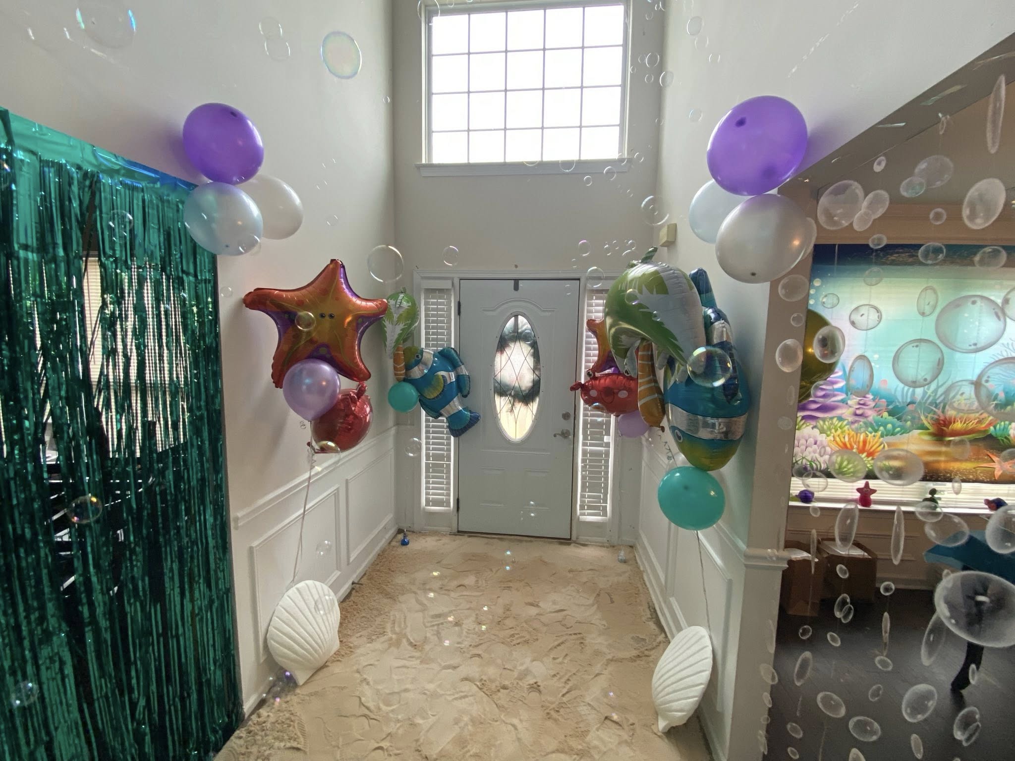 Entryway decorated for an under the sea party with beach sand, bubbles, and ocean animal balloons.