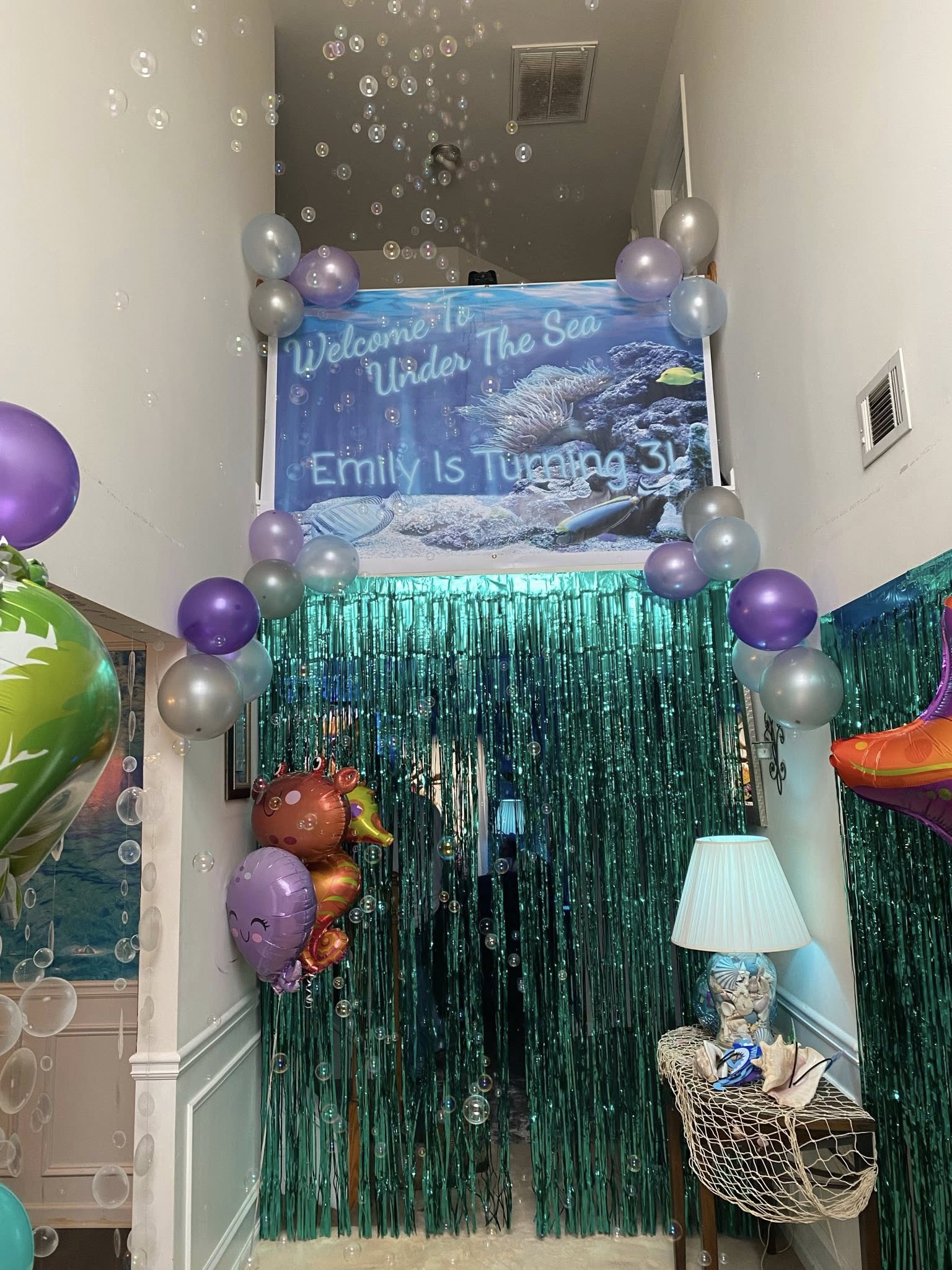 Under the sea themed 3rd birthday party decorations featuring a welcome banner, green fringe curtain, and balloons.