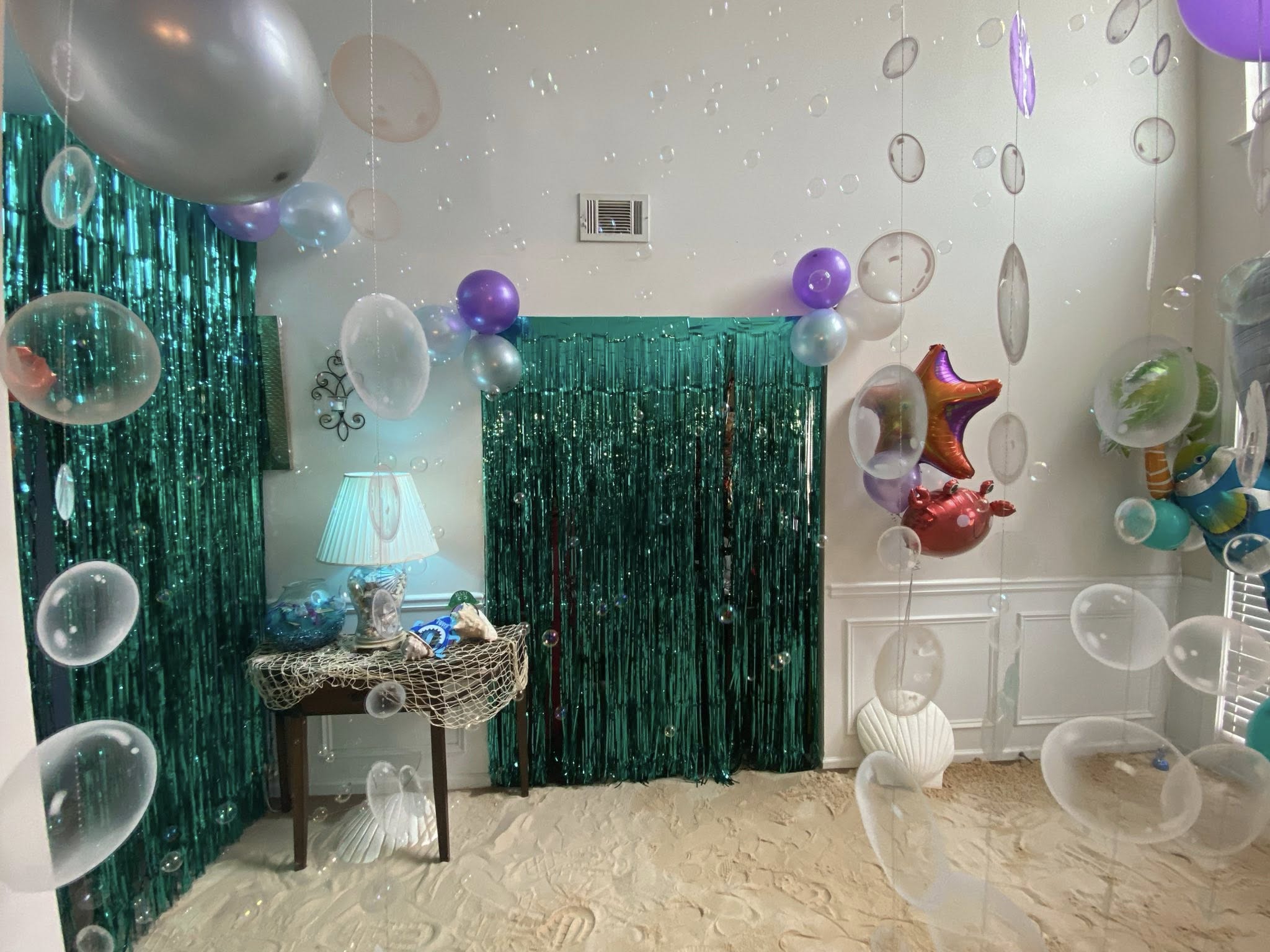 Under-the-sea themed party room decor with fringe curtains, floating bubbles, and ocean-themed balloons.