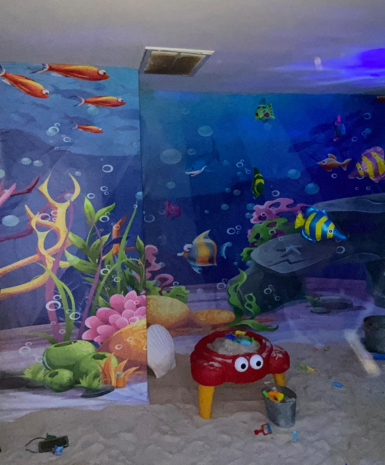 Childrens sand table shaped like a red crab set against an underwater ocean themed wall mural