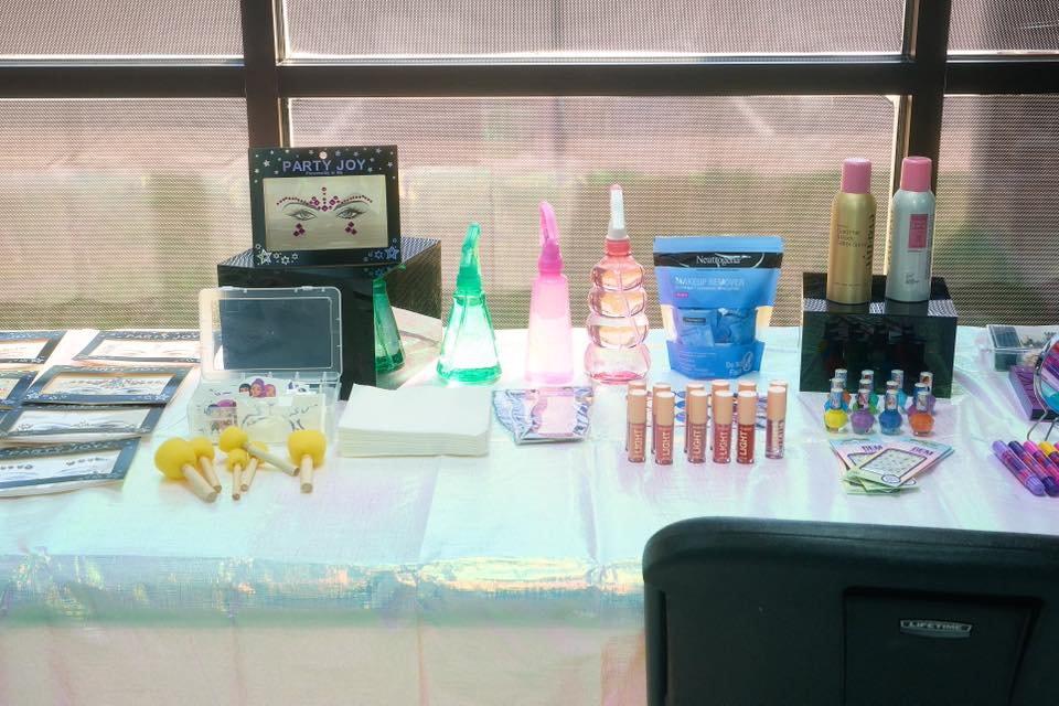 Makeup station setup with face gems, spray bottles, lip gloss tubes, nail polish, and makeup remover wipes