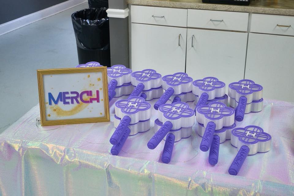 Display table of purple flower-shaped light sticks labeled with a Merch sign.