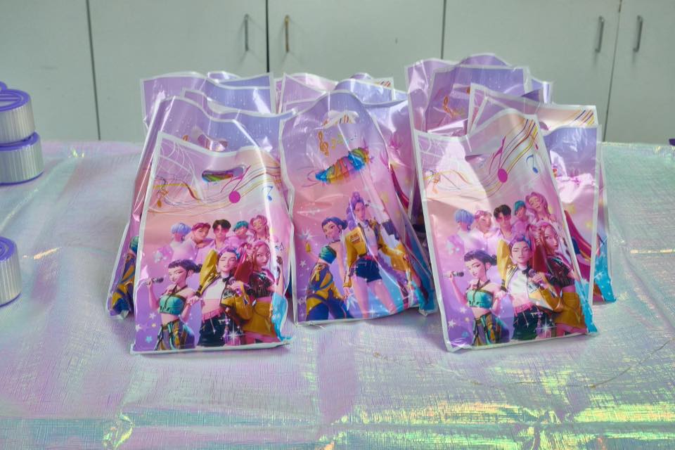 Stack of purple plastic party favor bags featuring an anime-style music group graphic