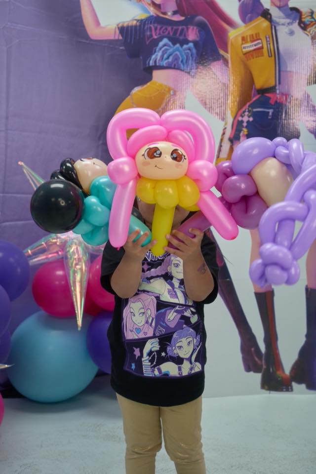 Child holding three colorful balloon dolls in front of an anime-themed party backdrop.