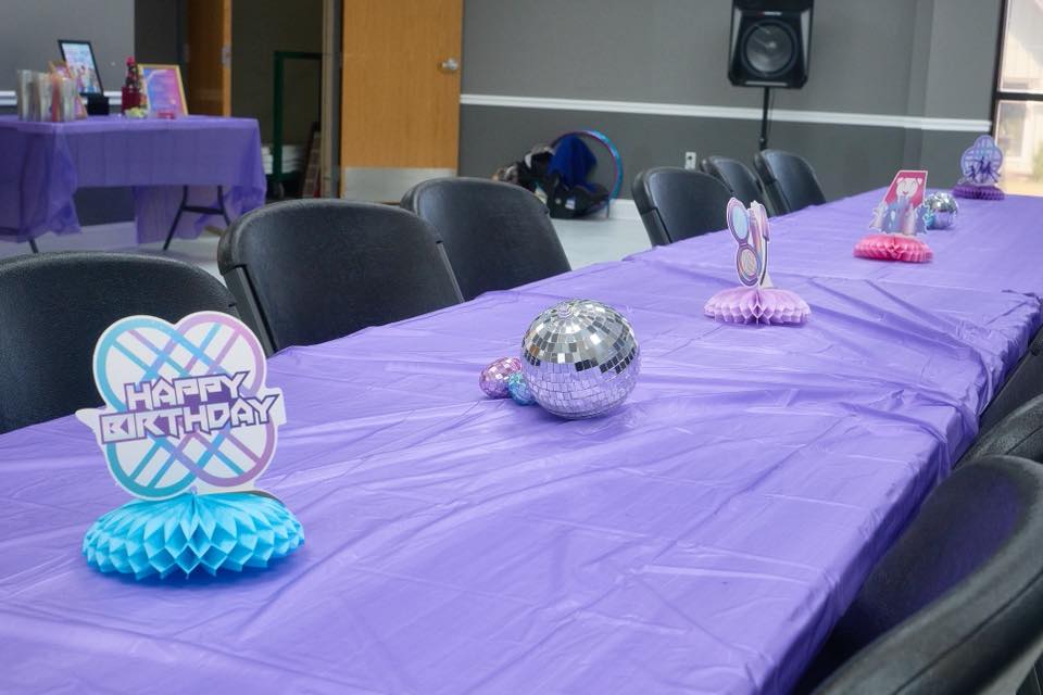 Long party table with purple tablecloth and Happy Birthday centerpiece decorations