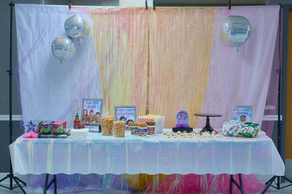 Table decorated for a themed party featuring a ramen bar, popcorn station, and Dr. Han's drink sign.