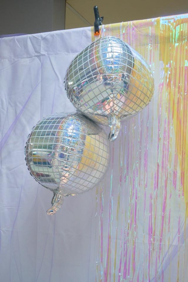 Two round disco ball foil balloons hanging against a backdrop