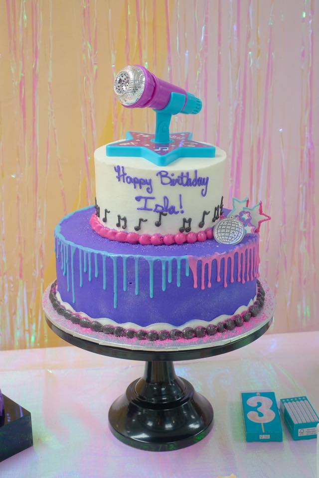 Two-tier purple and white birthday cake with music notes, a disco ball, and a microphone topper for Isla.