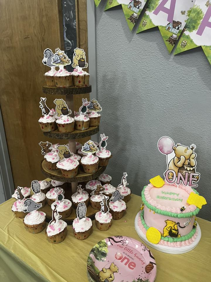 Winnie the Pooh themed first birthday dessert display with tiered cupcakes and a matching frosted cake.
