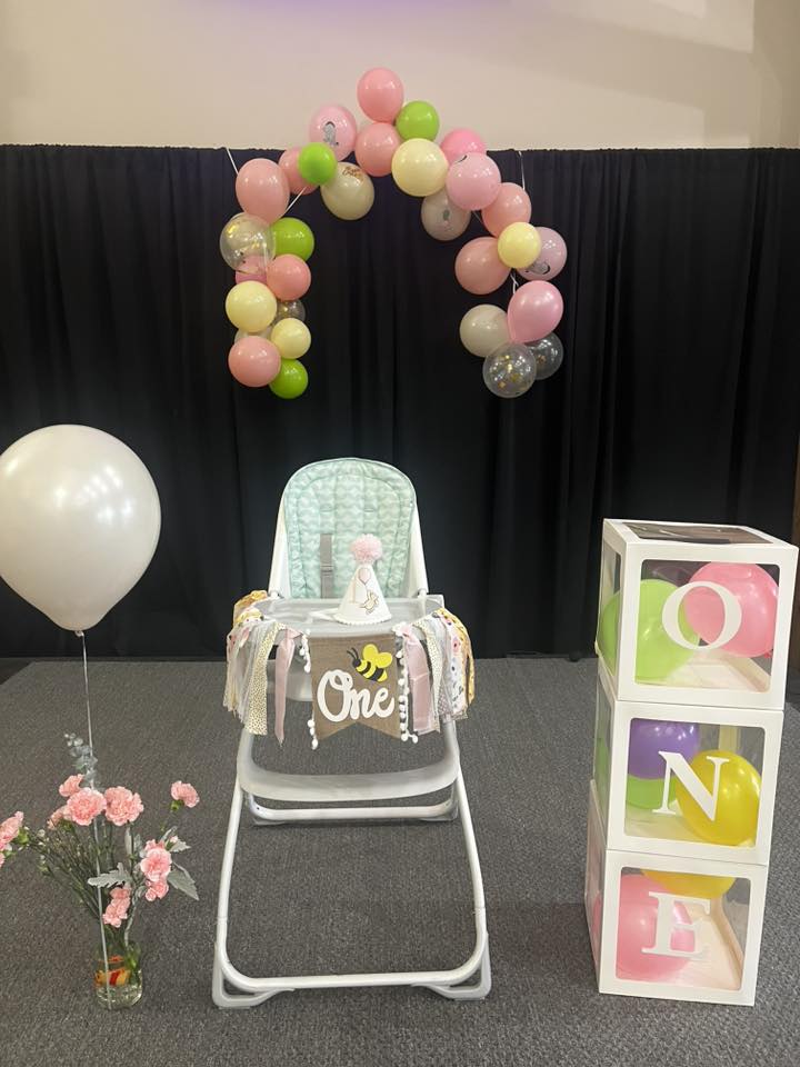 First birthday high chair decoration with bee-themed 'One' banner and balloon arch display