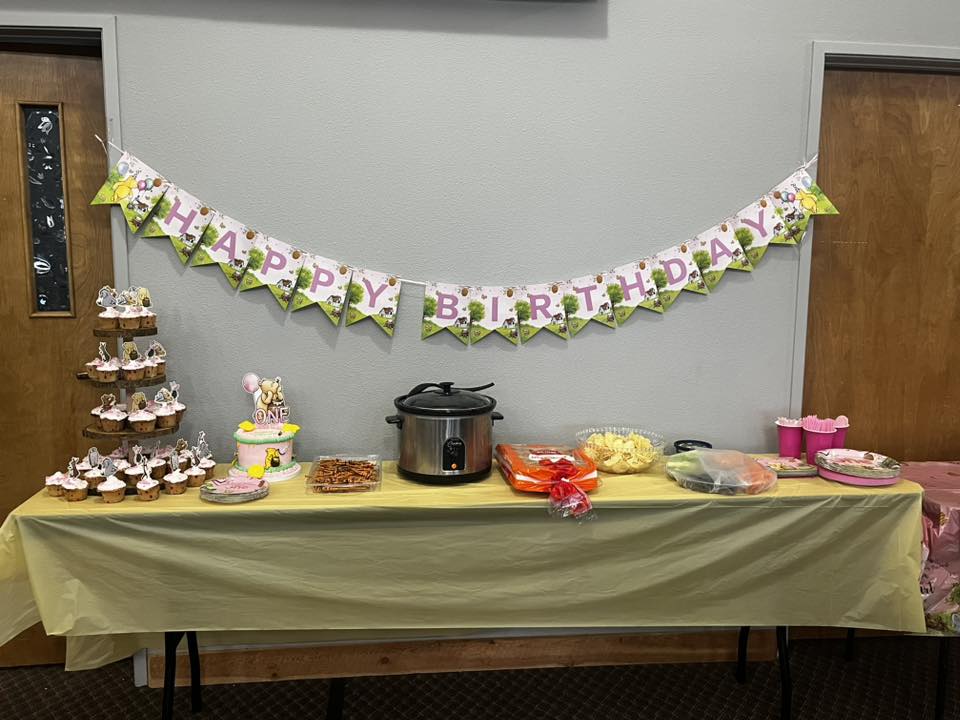 Table set up for a first birthday party with a happy birthday banner, cupcakes, and snacks.