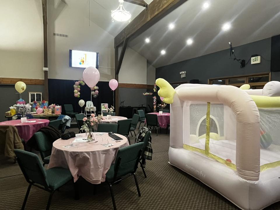 Event space set up with pink tablecloths, balloons, and an indoor bounce house for a celebration.