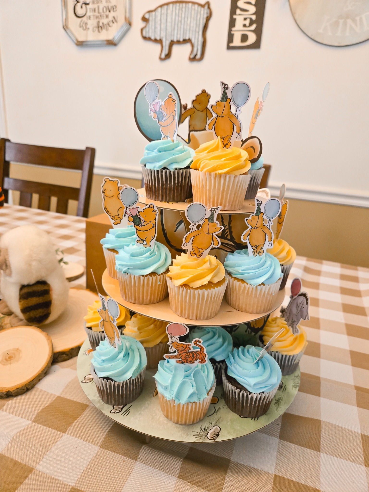 Three-tiered cupcake stand decorated with Winnie the Pooh character toppers and blue and yellow frosting.