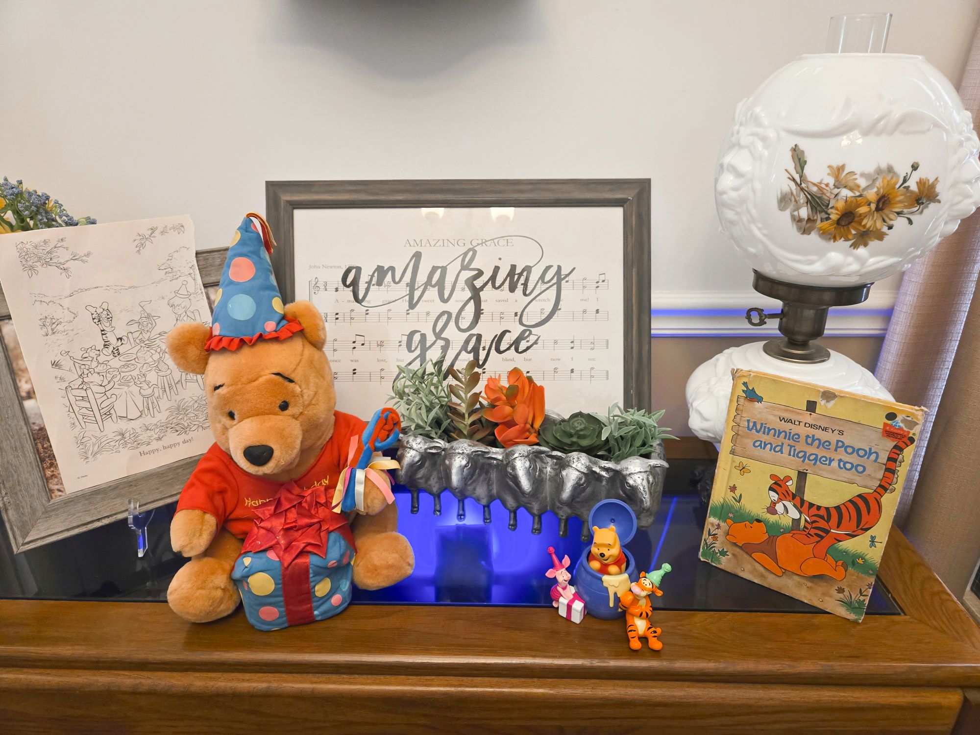 Winnie the Pooh plush, vintage book, and decorations arranged on a table with an Amazing Grace framed sheet music.