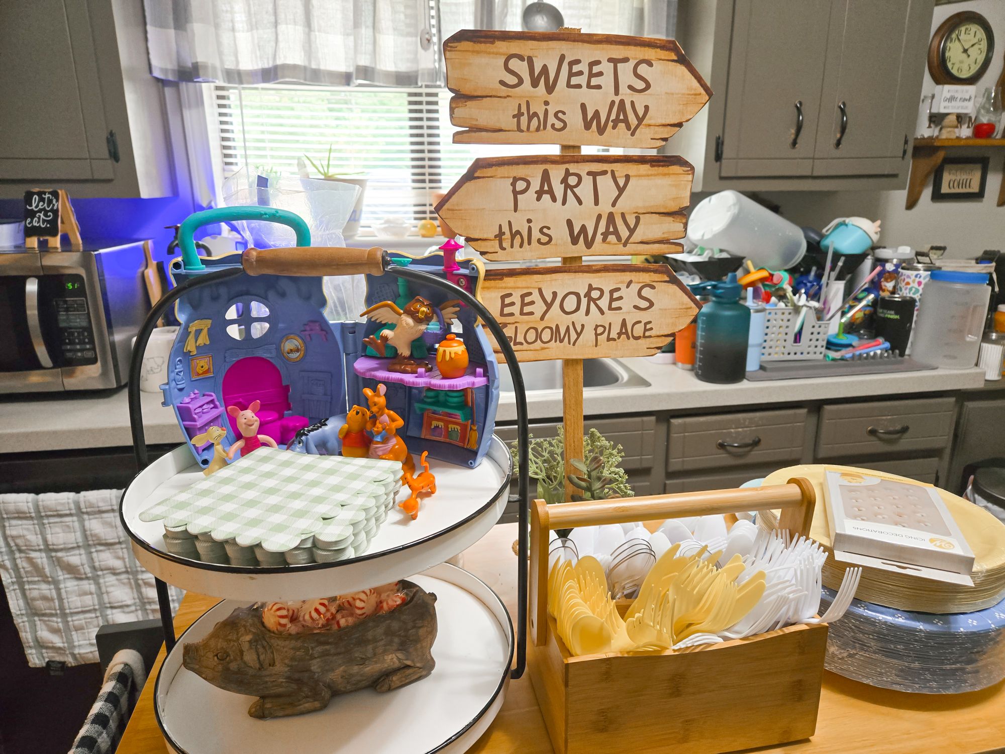 Winnie the Pooh themed party table decor featuring a tiered tray, wooden directional signs, and plastic utensils.