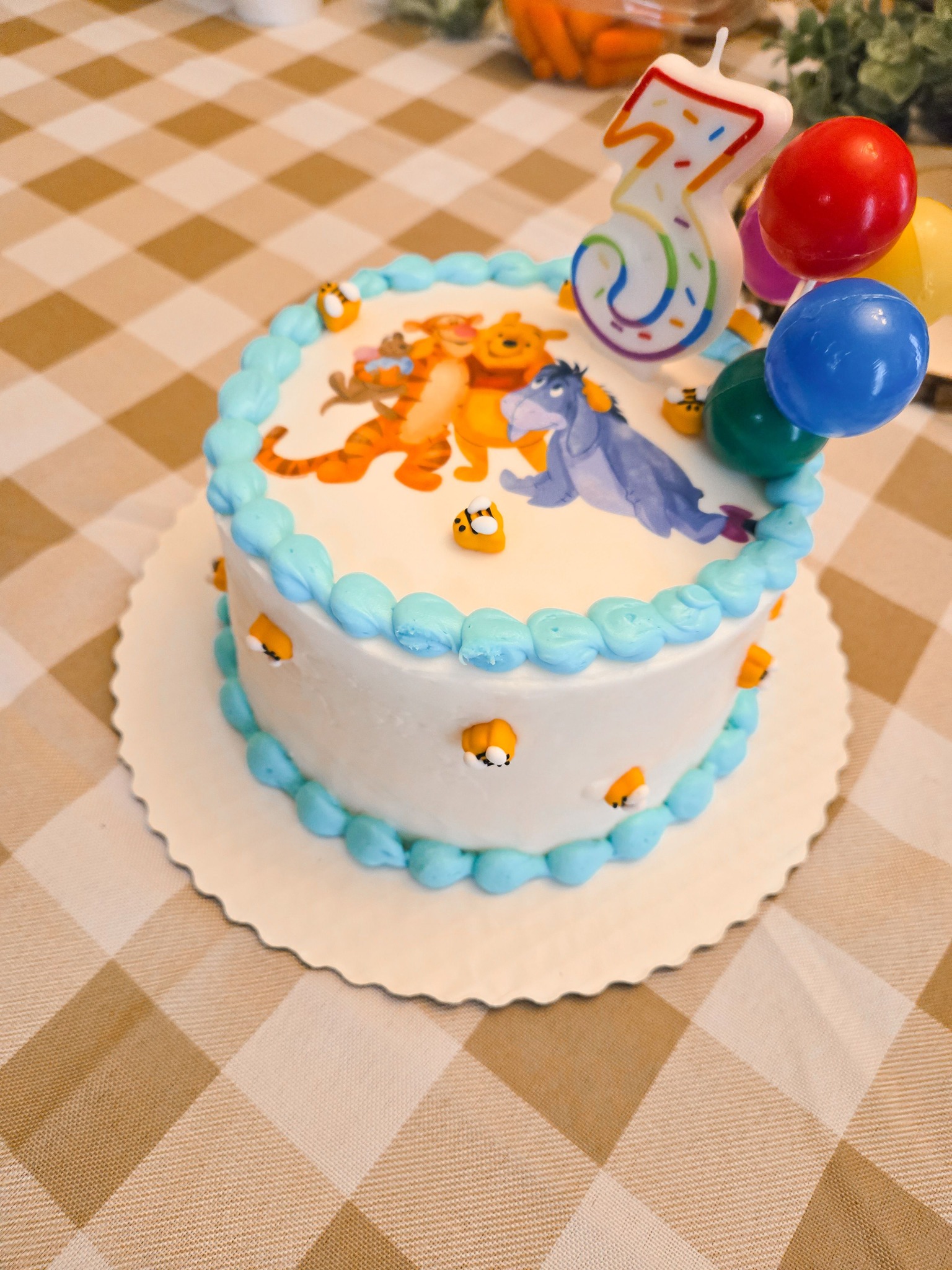 Round birthday cake with Winnie the Pooh decorations, blue frosting borders, bee accents, and a number 3 candle.