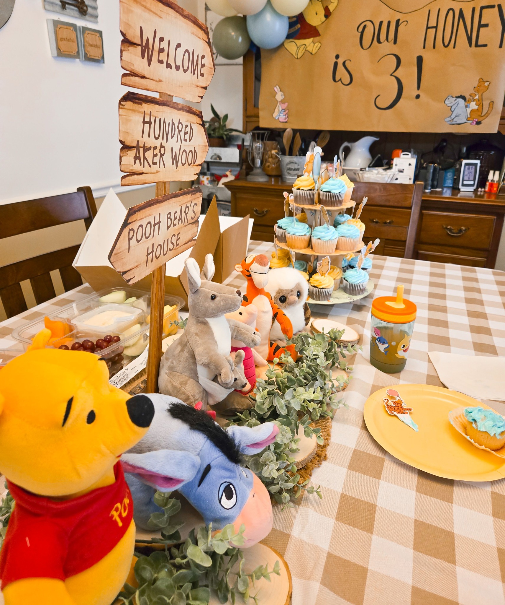 Winnie the Pooh themed birthday table centerpiece with plush characters and a cupcake stand.