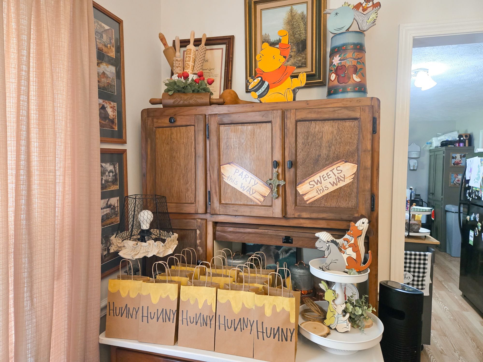 Table decorated with Winnie the Pooh Hunny treat bags and themed party signage on a wooden hutch.