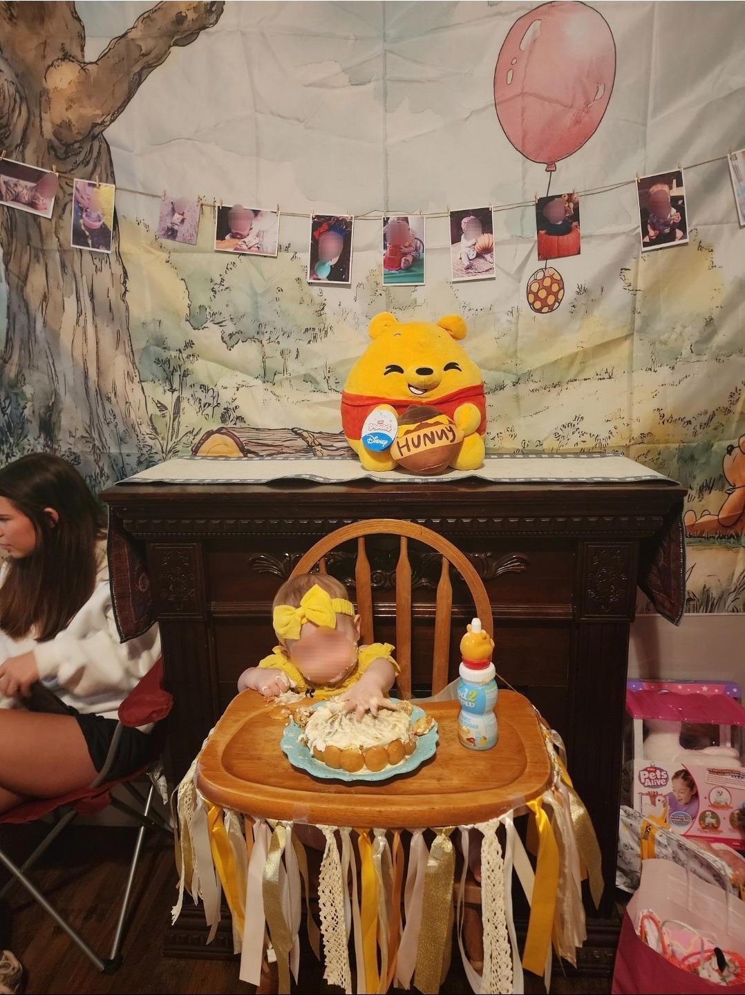 A baby wearing a yellow bow eating a smash cake at a Winnie the Pooh themed birthday party.