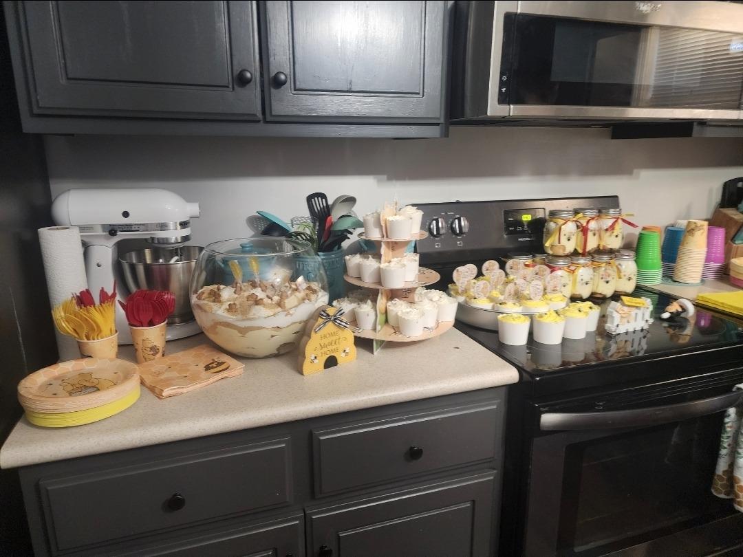 Winnie the Pooh themed party dessert table with cupcakes, trifle, and honeybee decor on a kitchen counter.