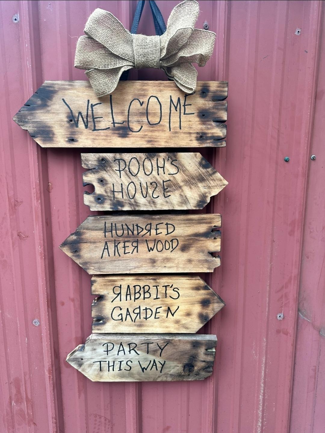 Hanging wooden rustic sign with burlap bow, featuring Winnie the Pooh inspired directional text.