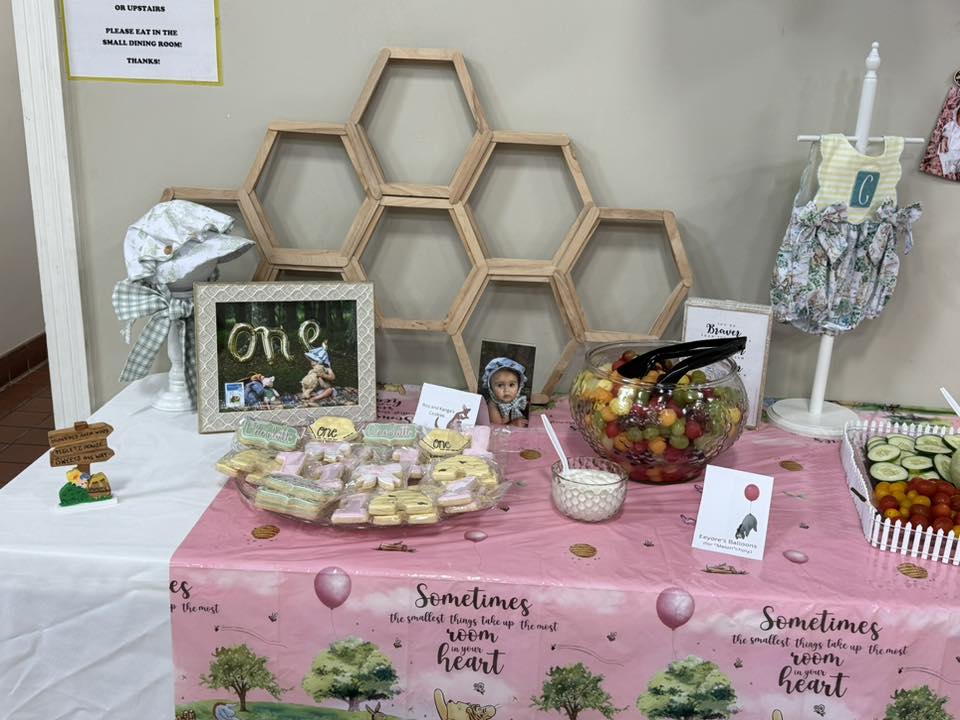 Winnie the Pooh themed birthday party food table featuring honeycomb decor, custom cookies, and fruit.