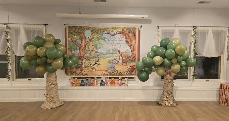 Two balloon trees decorated with green and gold balloons flanking a Winnie the Pooh display with plush characters.