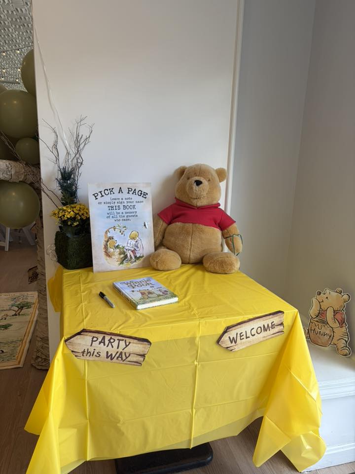 Winnie the Pooh guest book table with a teddy bear, guest sign-in book, and themed party decorations.