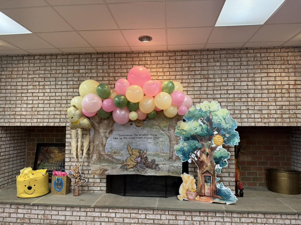 Winnie the Pooh themed party decorations featuring a balloon arch, a backdrop with Tigger and Pooh, and tree cutout.