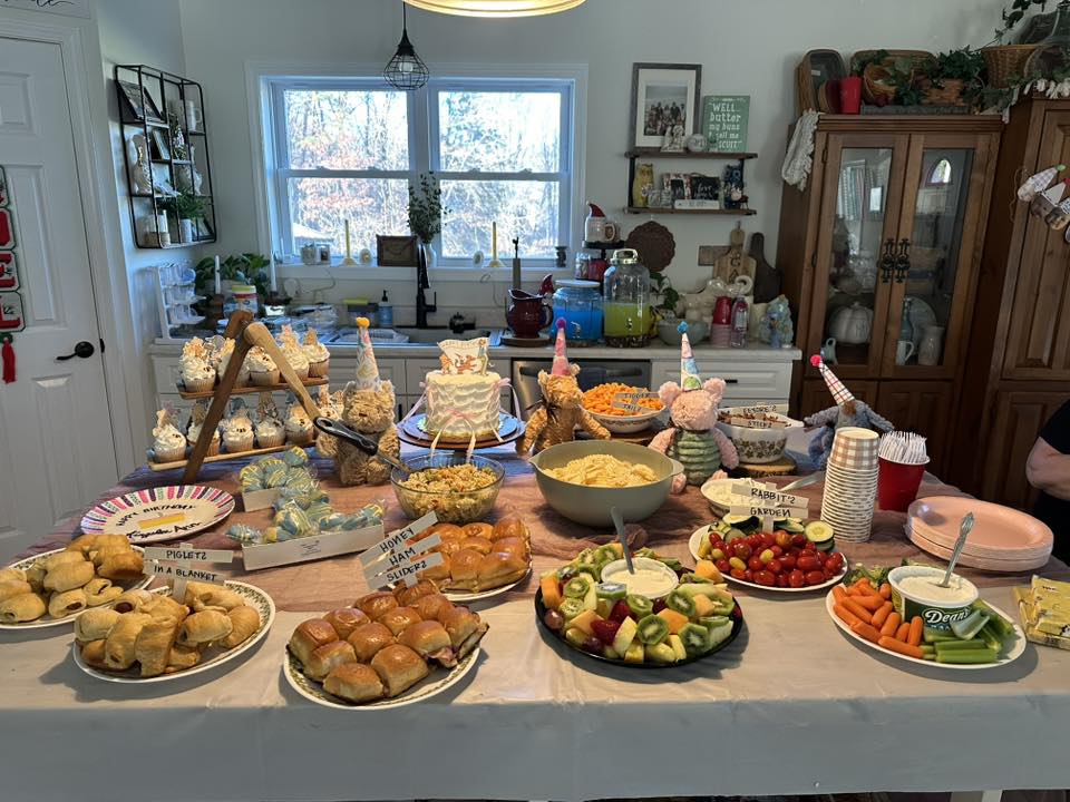 Winne the Pooh themed birthday party food spread with labeled dishes including Piglet in a Blanket and Rabbit's Garden.