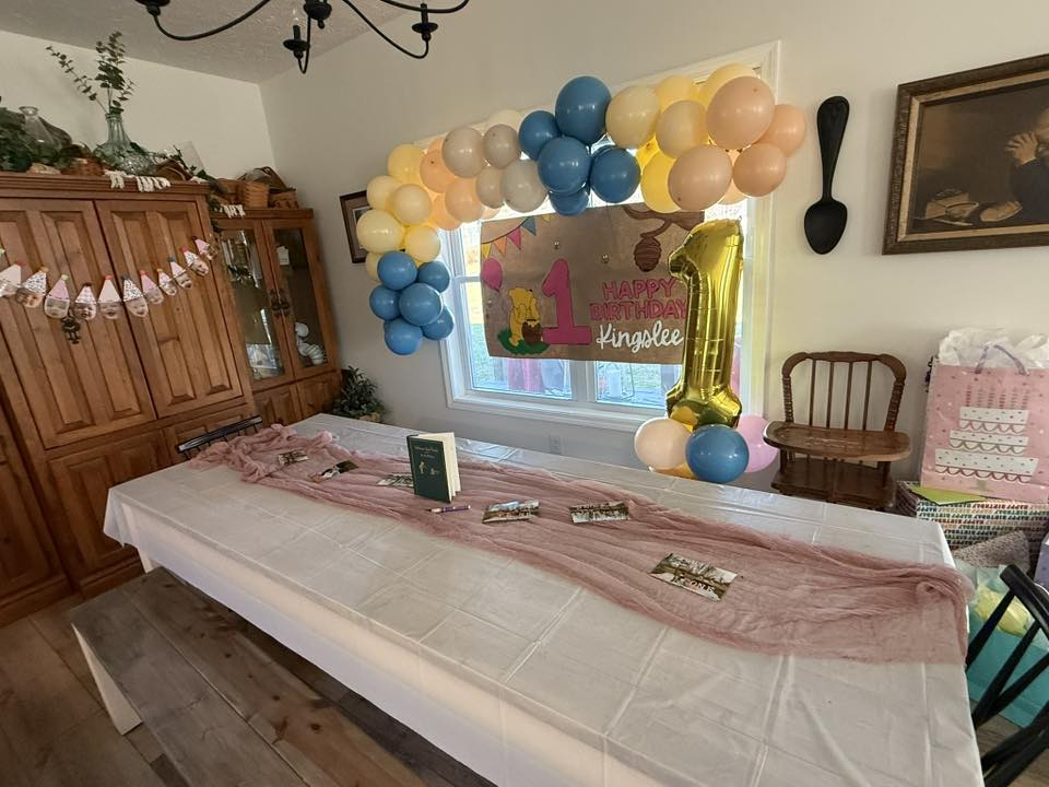 Dining table decorated for a first birthday with a Winnie the Pooh banner, balloons, and a gold number one balloon