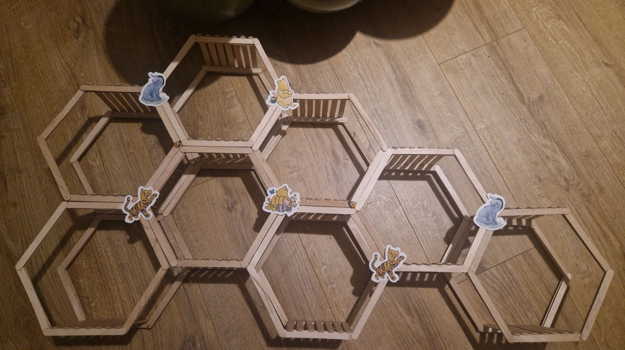 Honeycomb-shaped wooden popsicle stick wall shelf decorated with Winnie the Pooh and friends stickers.