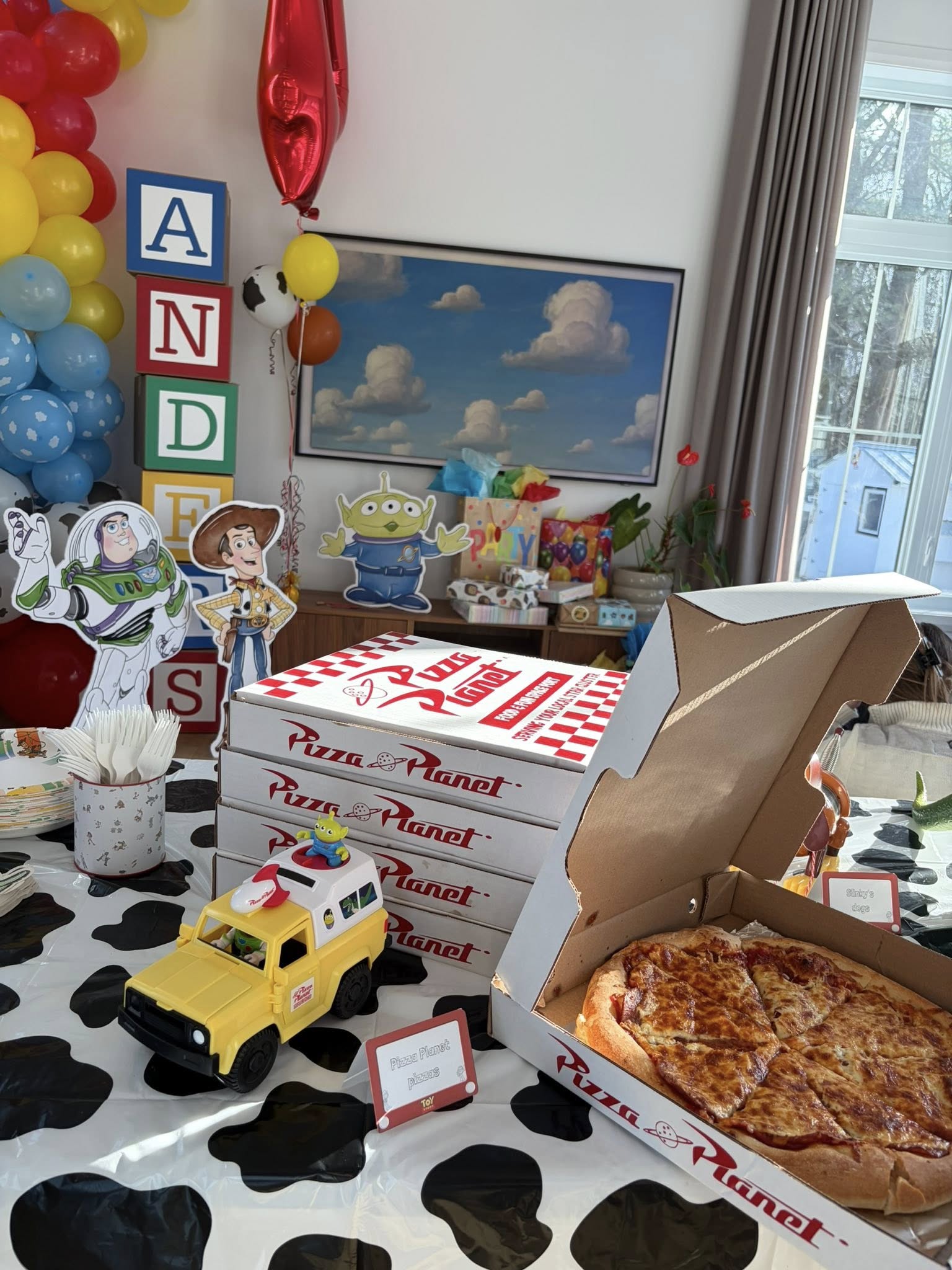 Toy Story themed party table with stacked Pizza Planet pizza boxes, a Pizza Planet delivery truck, and party decor.