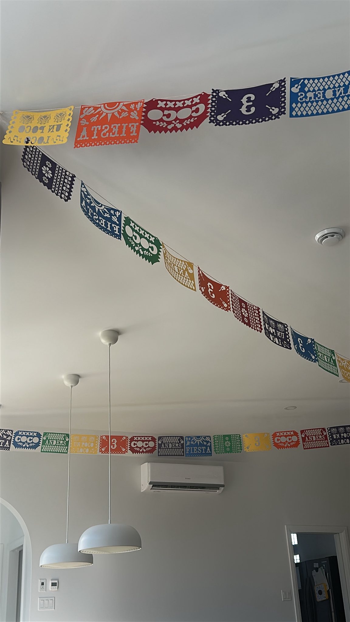 Colorful Coco-themed Mexican paper banner hanging on a white ceiling.