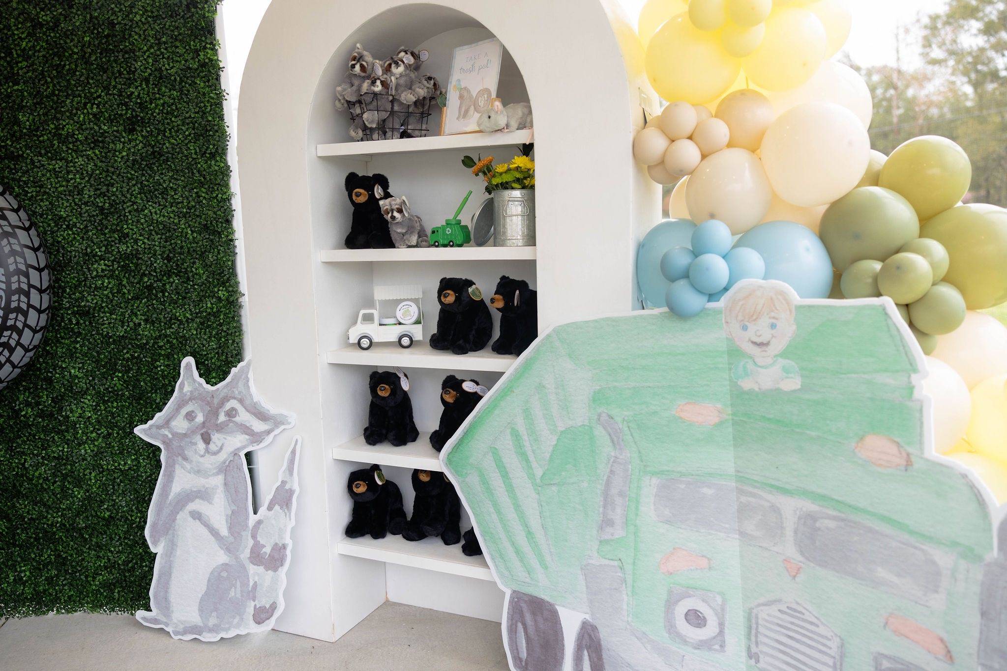 Display shelves featuring plush black bear toys, a small toy trash truck, and raccoon party decorations.