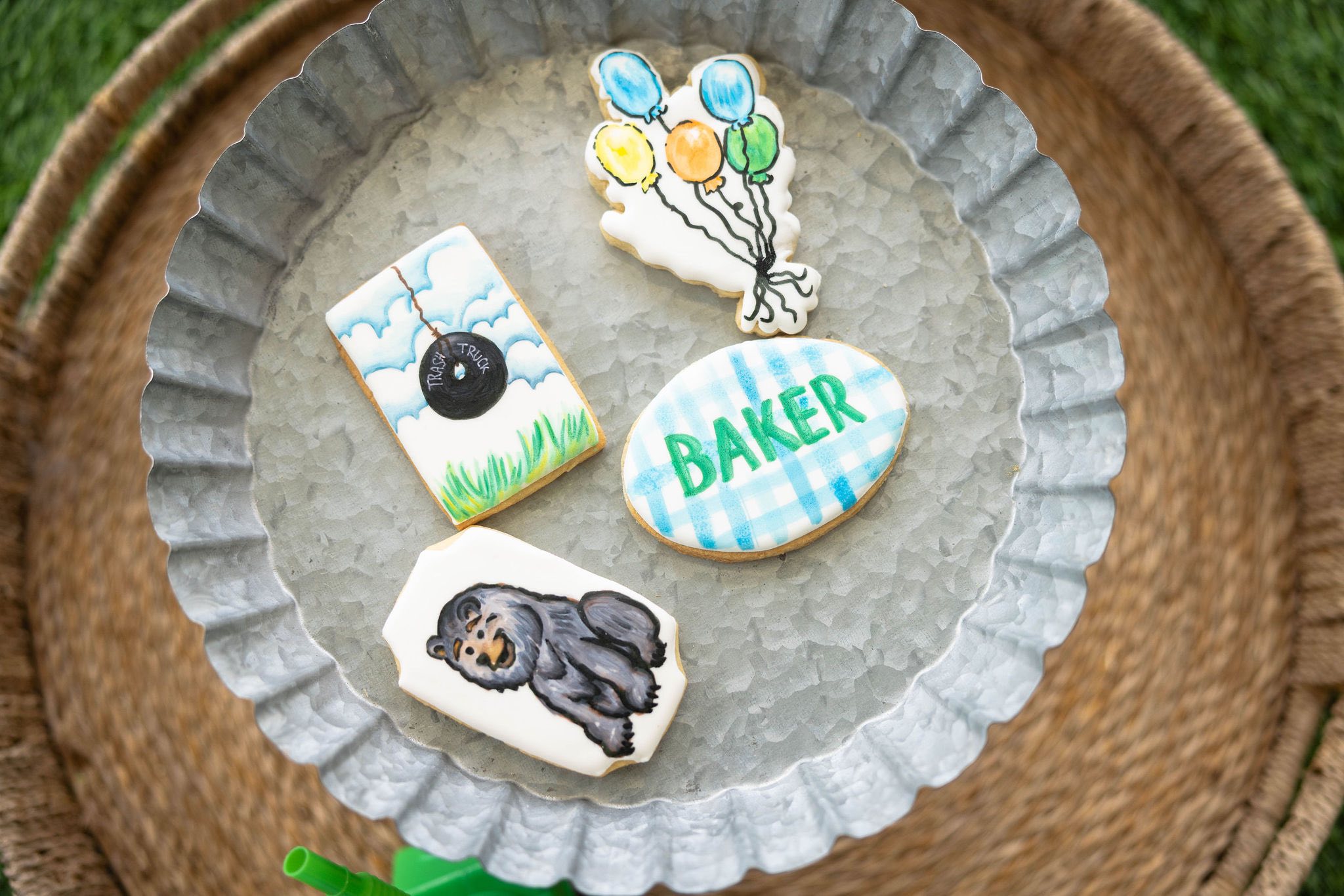 Decorated sugar cookies featuring a trash truck, colorful balloons, the name Baker, and a bear on a metal tray.