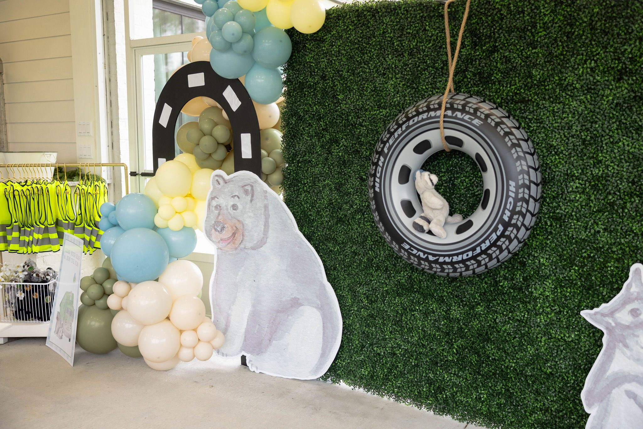Bear themed birthday party backdrop with a balloon arch, hanging tire prop, and bear cutout.