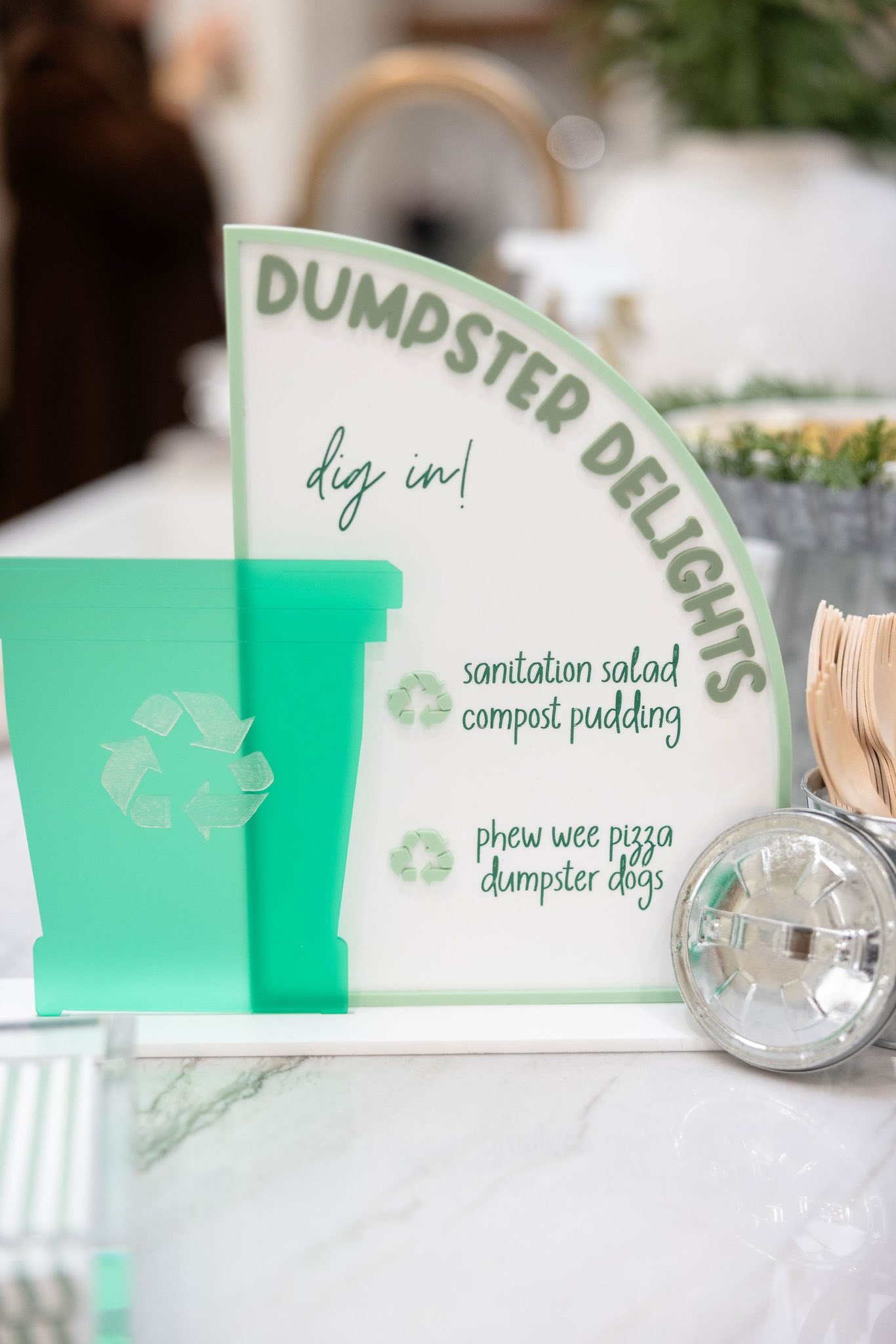 A decorative Dumpster Delights sign listing food items like sanitation salad and compost pudding.