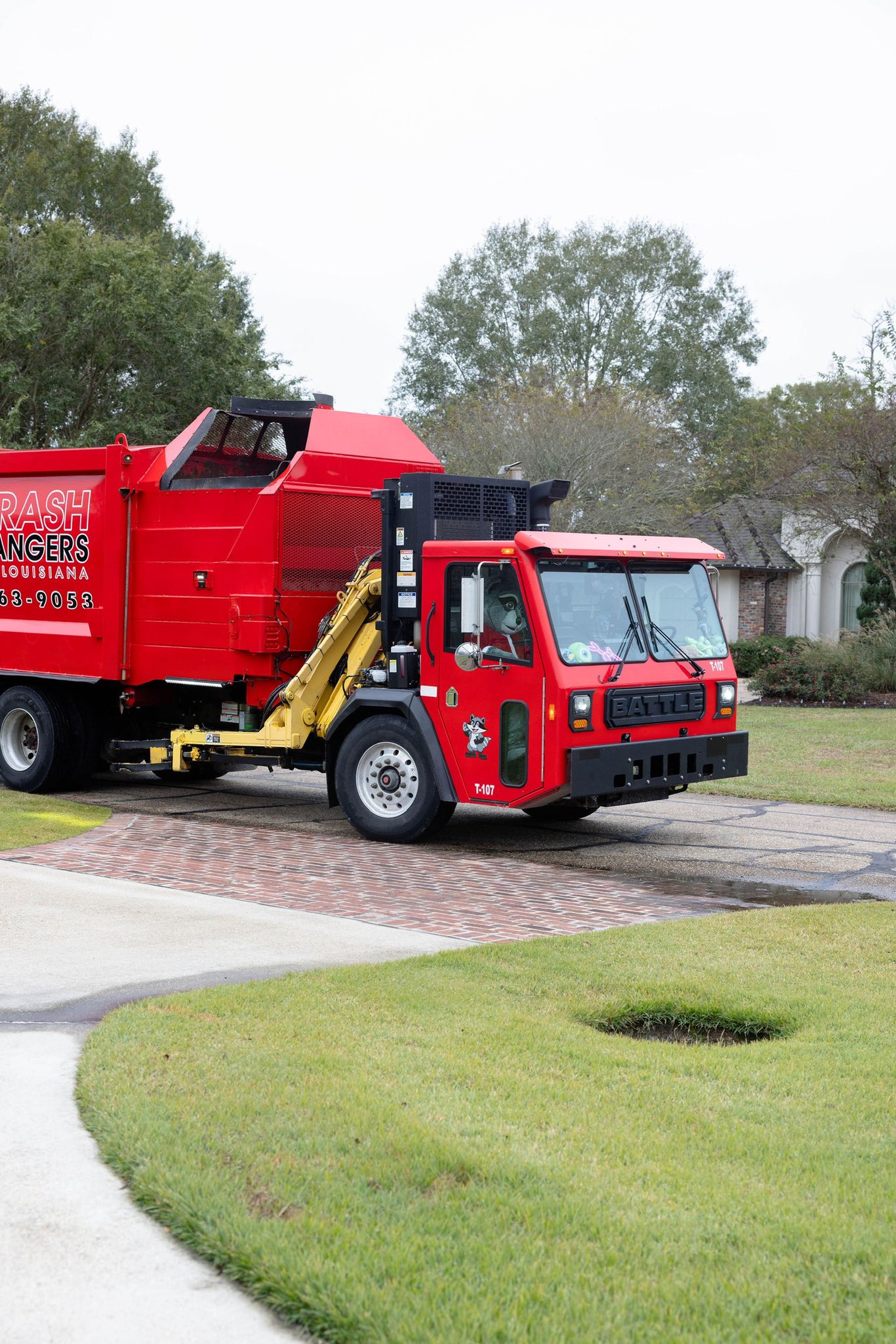 Bright red Trash Rangers garbage truck driving on a residential driveway.