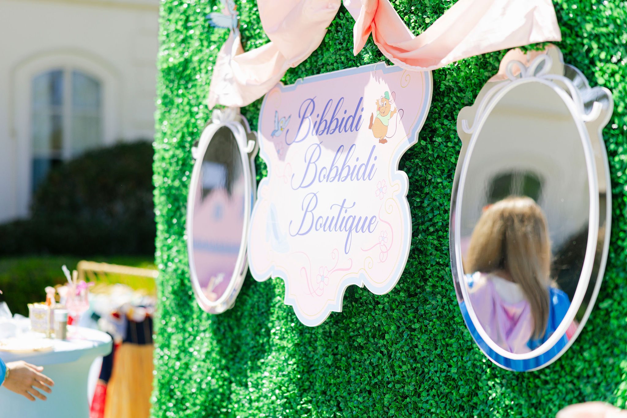 Bibbidi Bobbidi Boutique sign mounted on a green hedge wall with decorative mirrors
