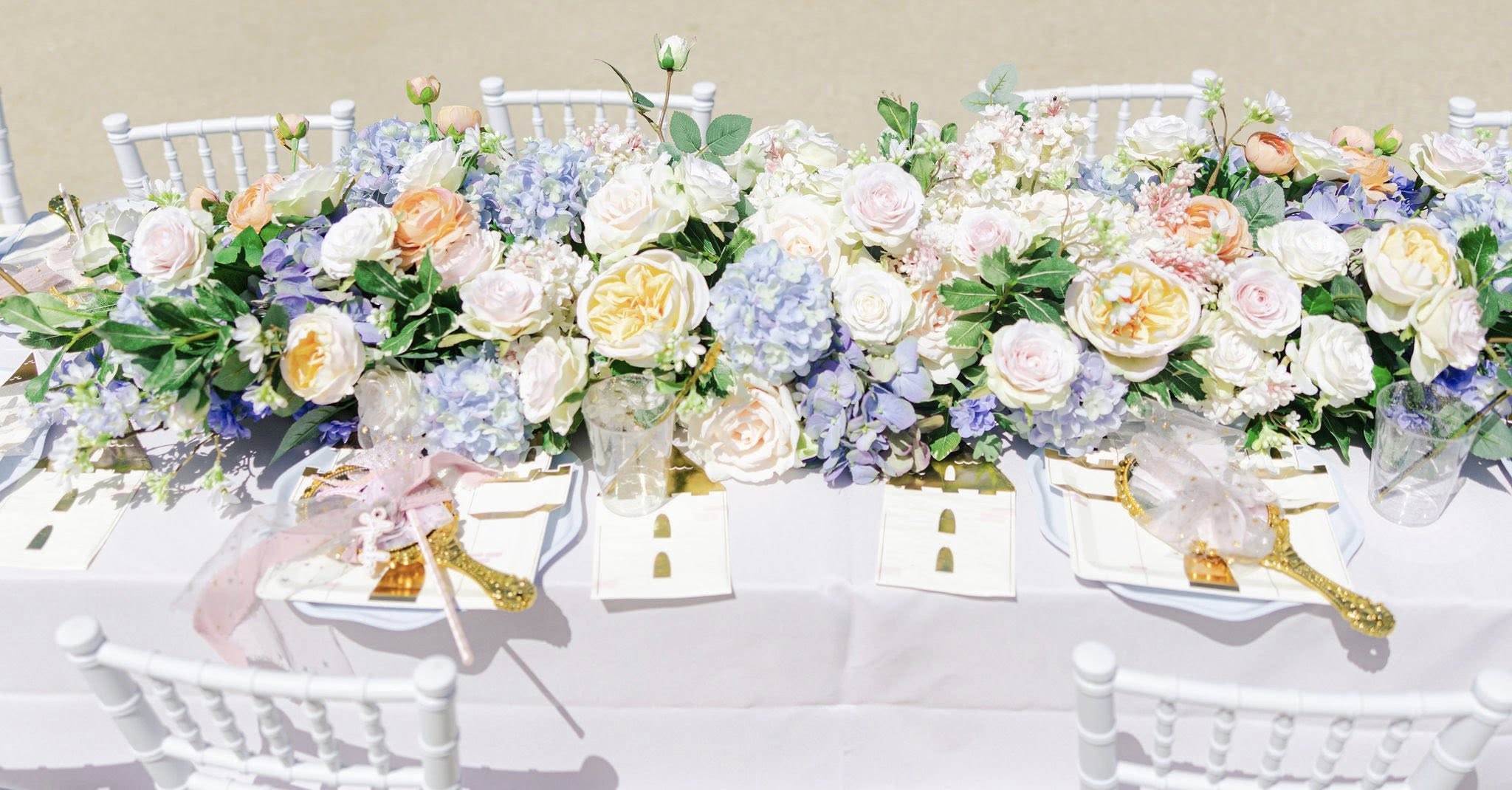 Dining table decorated with an elaborate floral runner of pastel roses and blue hydrangeas for an event